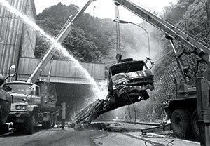 <b>1979年7月11日夜、静岡県焼津市の東名高速・日本坂トンネル下り線（全長2045メートル）内で起きた玉突き衝突から始まった炎上は、一昼夜たっても鎮火に至らなかった。写真は水をかけながら搬出されるトラック</b>（写真：読売新聞/アフロ）