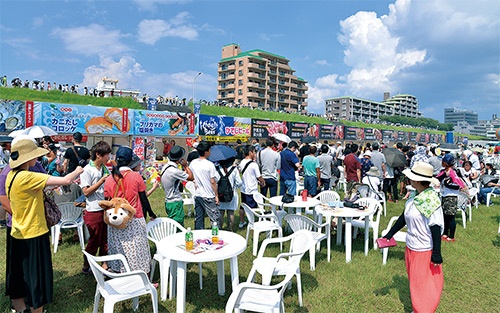<b>7月17日に宮崎市内の大淀川の河川敷で開催された「ふるまい宮崎」の会場の当日の様子。会場奥に見える土手の上には、入場を待つ人の列ができていた</b>