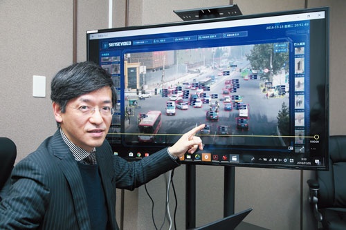 <span class="fontBold">中国・西安の監視カメラ映像を示す、センスタイムジャパンの勞世竑社長。クルマのナンバーや属性を瞬時に把握できる</span>(写真=山田 哲也)