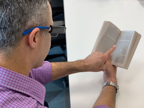 オーカムが開発したデバイスをメガネに装着し、文章を指さすと文字を読み上げる