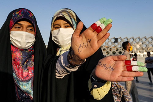 ライシ師を支持するイランの市民。人さし指と中指はイランの国旗と同じ色にペインティングしている。手のひらの文字は「ロウハニ、バイバイ」と書かれている（写真：AFP/アフロ）