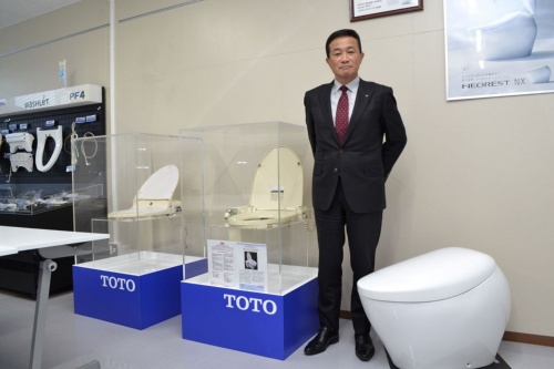 ウォシュレット1号機と最新型ネオレストNXの間に立つ林良祐TOTO専務執行役員
