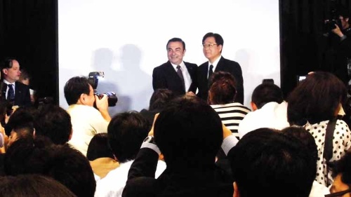 三菱自・益子社長と握手し、取材陣のカメラに笑顔を見せる日産・ゴーン社長