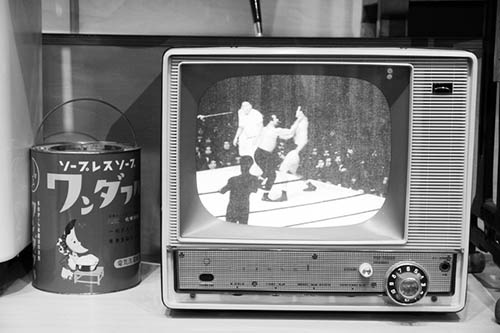 昭和30年代の白黒テレビ。当時のプロレス人気をけん引したレスラー、力道山は東京五輪開催の前年に亡くなった。左は洗濯機用の粉石けんの容器。（写真:PIXTA）