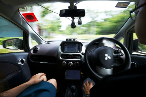 シンガポールの自動運転タクシーの室内。右側に座っている男性は、ステアリング（ハンドル）から手を離し、手を膝の上に置いたまま。このタクシーを運営しているヌートノミー社の担当者は、自動走行のタクシーの数が増えれば、街中を走る車の数を大幅削減できると語った。（写真：AP／アフロ）