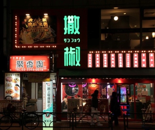赤の外装に、緑色で「撒椒」と書かれた大きなネオンサインが浮かび上がる外観。隣接する建物の2階にも他の中華料理店が入っている