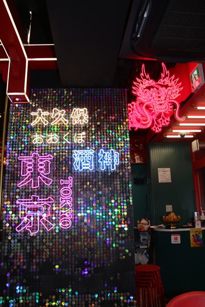 キラキラ銀色にデコされた柱には「東京」「大久保」「酒神」といった漢字のネオンサインとショッキングピンクで描かれたドラゴンのネオンがつるされている