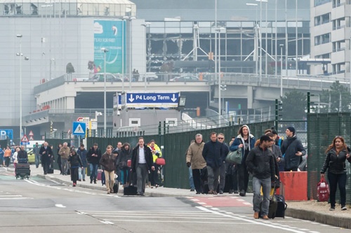 ブリュッセル国際空港から歩いて避難する人々。奥には爆破されたターミナルビルが見える（写真：AP/アフロ）