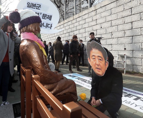 1月4日、釜山の日本総領事館前。慰安婦像の前で安倍首相のお面を付け、ひざまずくパフォーマンスが（写真：YONHAP NEWS/アフロ）