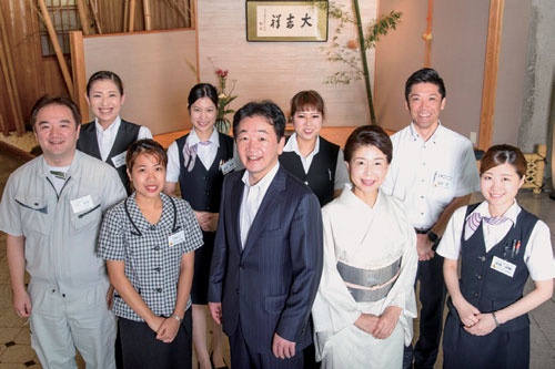 山口専務(前列中央)と女将(その右)を囲んで社員が集合。休みが増えて、気持ちに余裕が生まれたことで、今まで以上に明るい笑顔でお客をもてなせるようになった(写真:山岸政仁)