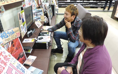 ソファ席に座って接客する宇都宮本店の竹原賢治店長(奥)。印刷する写真データを一緒に選んでいる