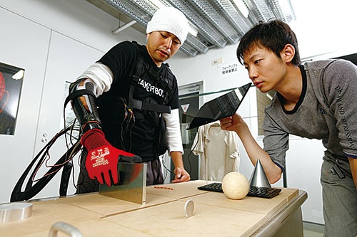 「サイバスロン」では様々なモノをつかみ移動させる競技も。右はソフト開発などを手掛ける粕谷氏(写真=竹井 俊晴)