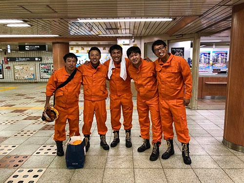 東急電鉄、夜の三軒茶屋駅に、揃いの「オレンジ色のつなぎ」で集合しました