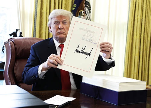 12月22日、米ホワイトハウスの大統領執務室で税制改革法案に署名、文書を掲げるドナルド・トランプ米大統領（写真：AP/アフロ）