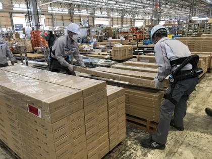 ロボットスーツを装着して荷物を運ぶ大和ハウス工業竜ヶ崎工場の作業員。1日に200～250ケース運ぶという床材の重さは30kgにもなる（下）