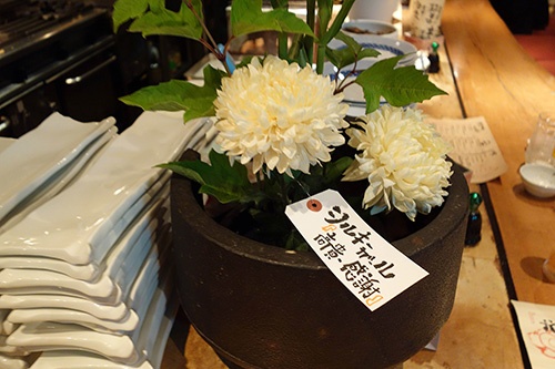 宇野氏がアドバイスする金沢の居酒屋のカウンターに置かれた生け花。花の種類や花言葉を書いた荷札を付けて、会話のきっかけをつくる