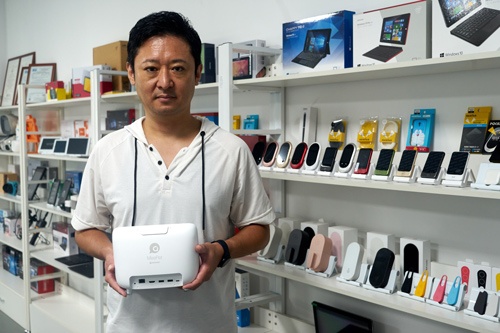 JENESISの藤岡社長。手にしているのはソースネクストから発売予定のリモート会議端末KAIGIO MeePet。新型コロナ禍でICT端末の需要は高まっている