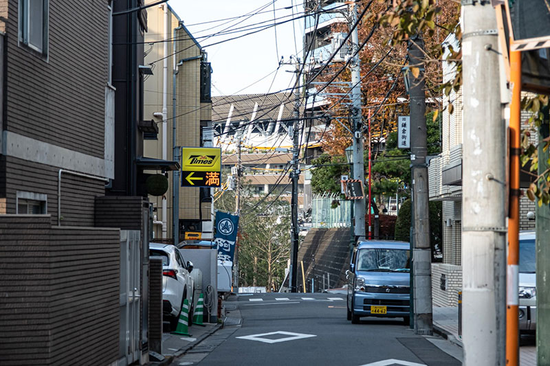 勢揃坂の上から国立競技場が顔を出す。先に見える横断歩道の先はさらに下っている。右手の電柱に「旧鎌倉街道」とあるのが見える