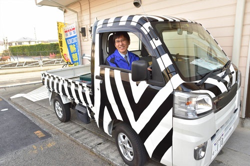 訪問営業車に乗るライフテクト イトウの伊藤社長。アドバイスを受けた東京都町田市の家電店ヤマグチに倣って、車の外装をゼブラ柄にしている(写真=菊池一郎、以下同)