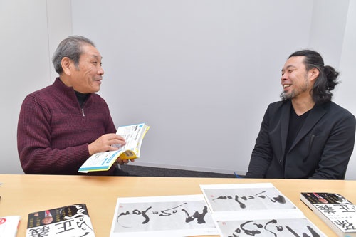 井上篤夫さん(左)が手にしているのは、前田鎌利さん(右)の著書『プレゼン資料のデザイン図鑑』。手前に見える井上さんの著書『孫正義 事業家の精神』の表紙には、鎌利さんが揮毫を寄せている(写真:菊池一郎)