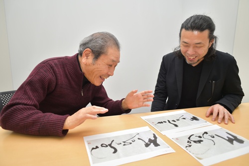井上さんの著書の表紙に、鎌利さんが寄せた揮毫を眺めながら語り合う。孫社長に3案を提示し、選んだ1案は「孫さんのシャープさと柔らかさを表現した」(鎌利さん)という向かって左側の作品(写真:菊池一郎)